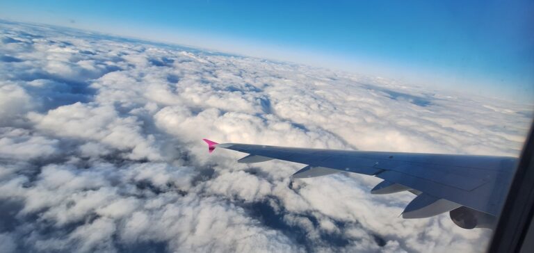 pink wingtip against a partly cloudy sky and horizon while flying