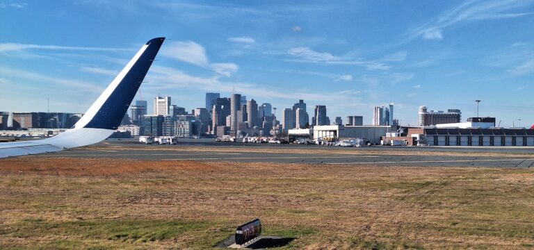 a plane wing on a runway with a city in the background